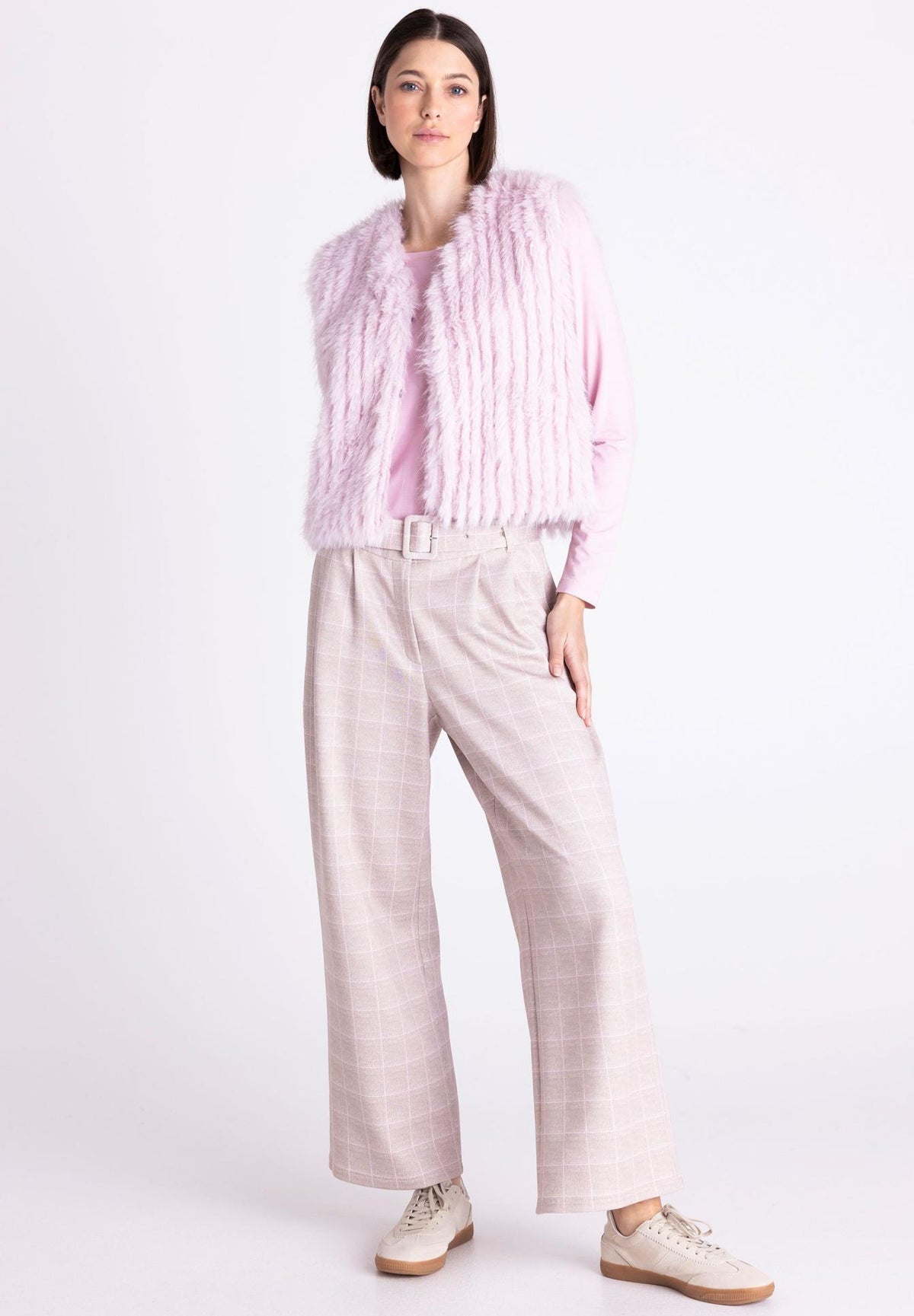 A model stands against a plain white studio background wearing a light pink fuzzy cropped vest over a matching pink top, wide-leg light pink plaid trousers, and beige sneakers.