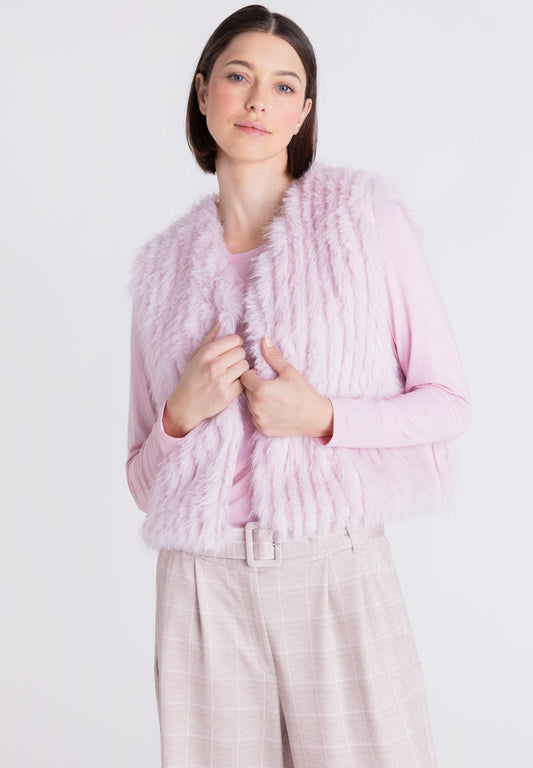 A woman wearing a light pink faux fur vest over a matching pink top and light pink plaid trousers, photographed against a plain white studio background.