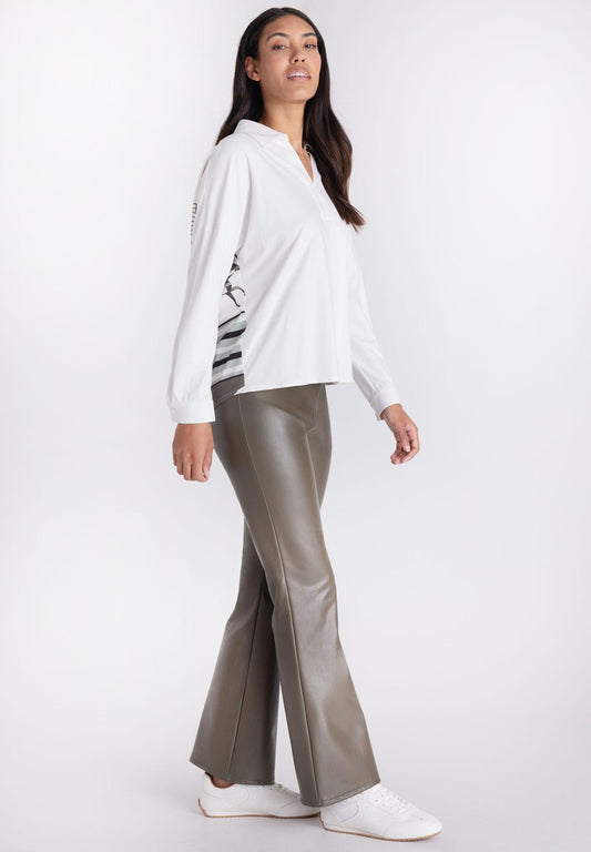 A woman modeling a white long-sleeve collared blouse with a black and white striped pattern on the lower sleeve, paired with metallic taupe pants, against a plain white studio background.