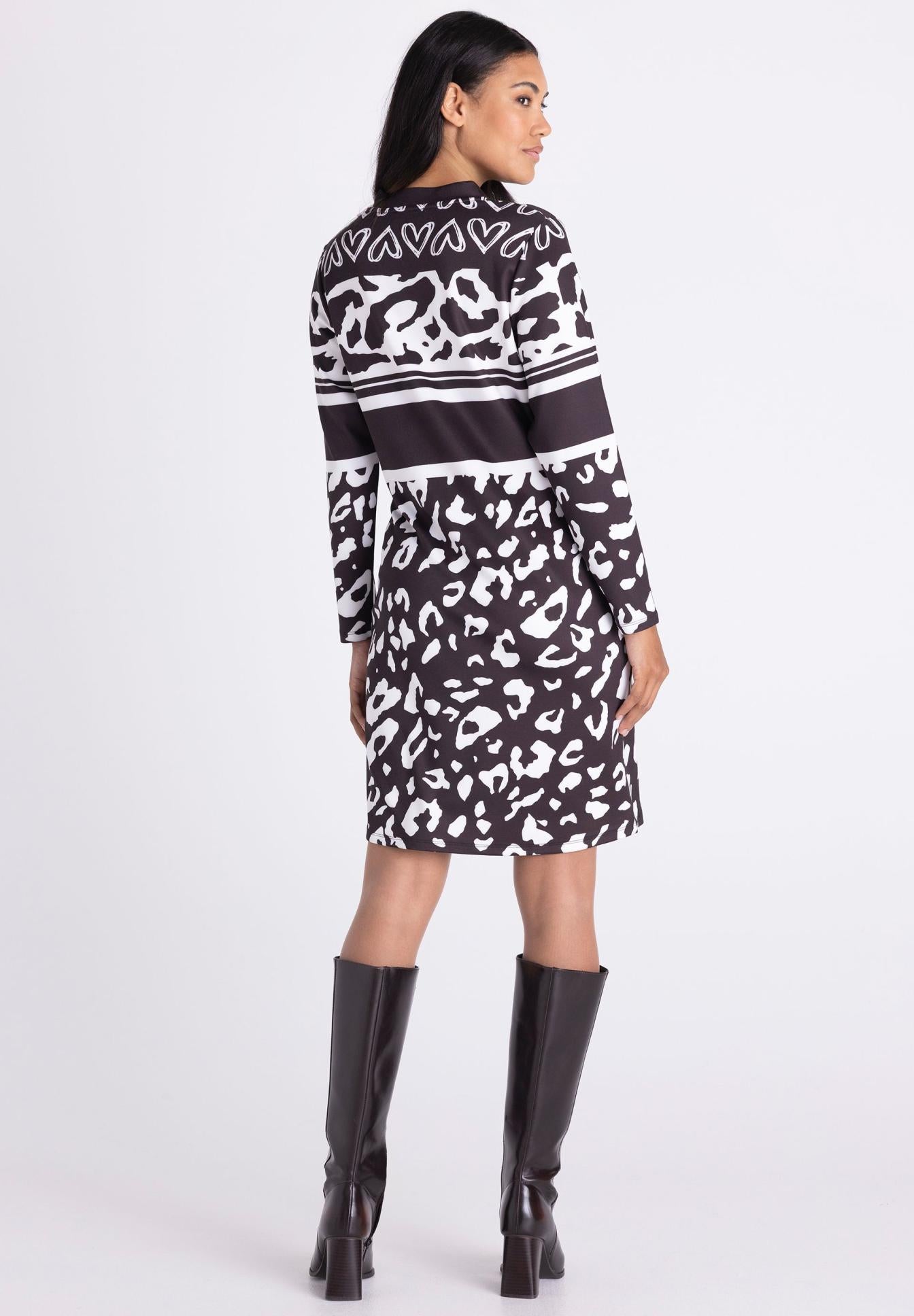 A woman shown from the back wearing a long-sleeve knee-length dress with a black and white abstract pattern, paired with black knee-high boots, against a light gray studio background.