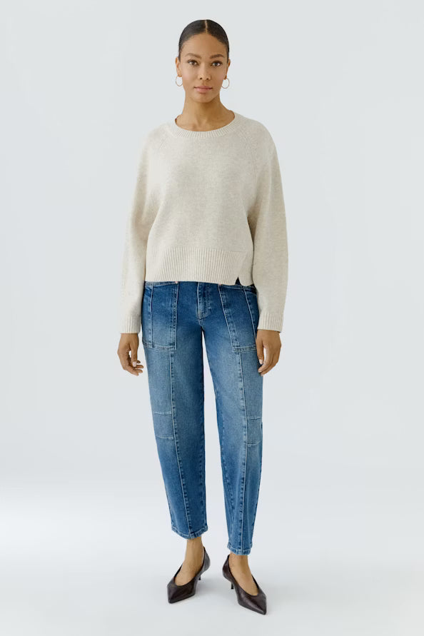 Woman wearing a beige sweater and blue jeans on a white background