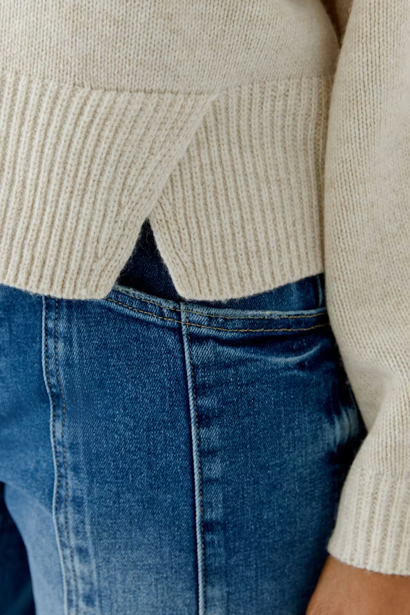 Close-up of a person wearing a beige sweater and blue jeans.