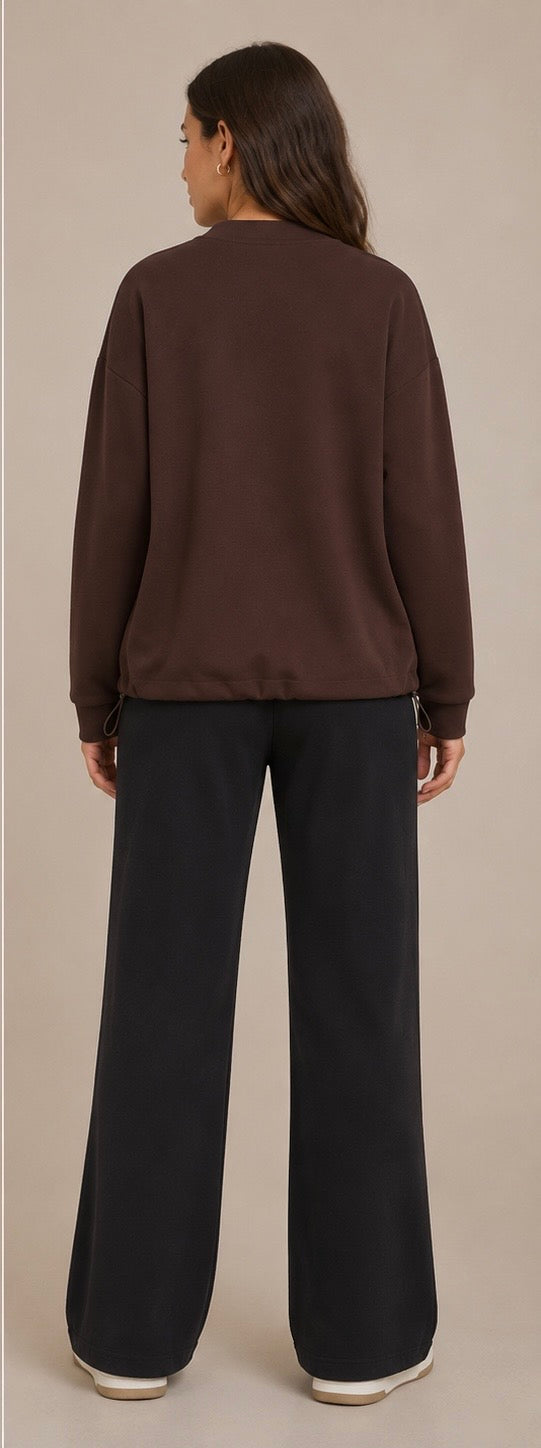 A woman shown from the back wearing a dark brown long-sleeve top and black wide-leg pants against a plain beige studio background.