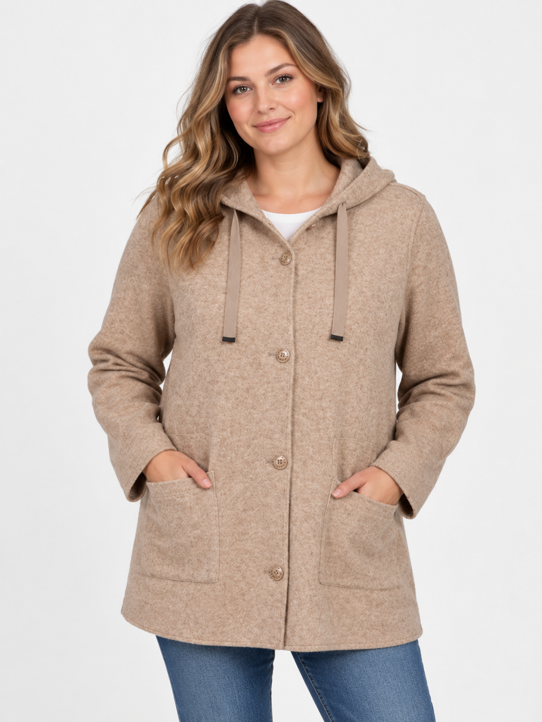A woman wearing a beige hooded button-front coat with drawstrings and front pockets, paired with blue jeans, against a plain light gray studio background.