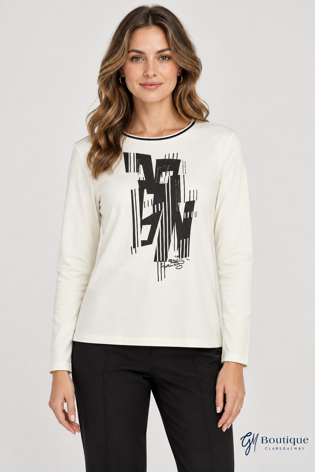 A woman modeling a cream long-sleeve crewneck top with a large black abstract graphic on the front, paired with black pants, against a light gray studio background.