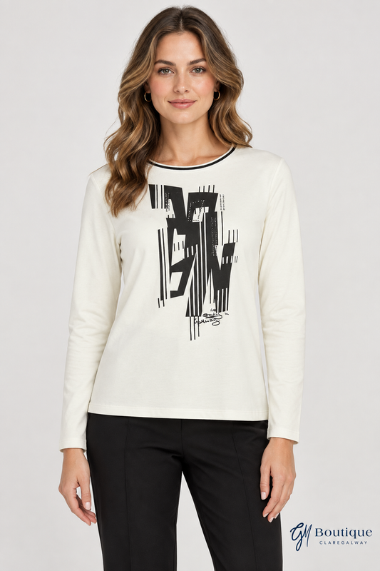 A woman modeling a cream long-sleeve crewneck top with a large black abstract graphic on the front, paired with black pants, against a light gray studio background.