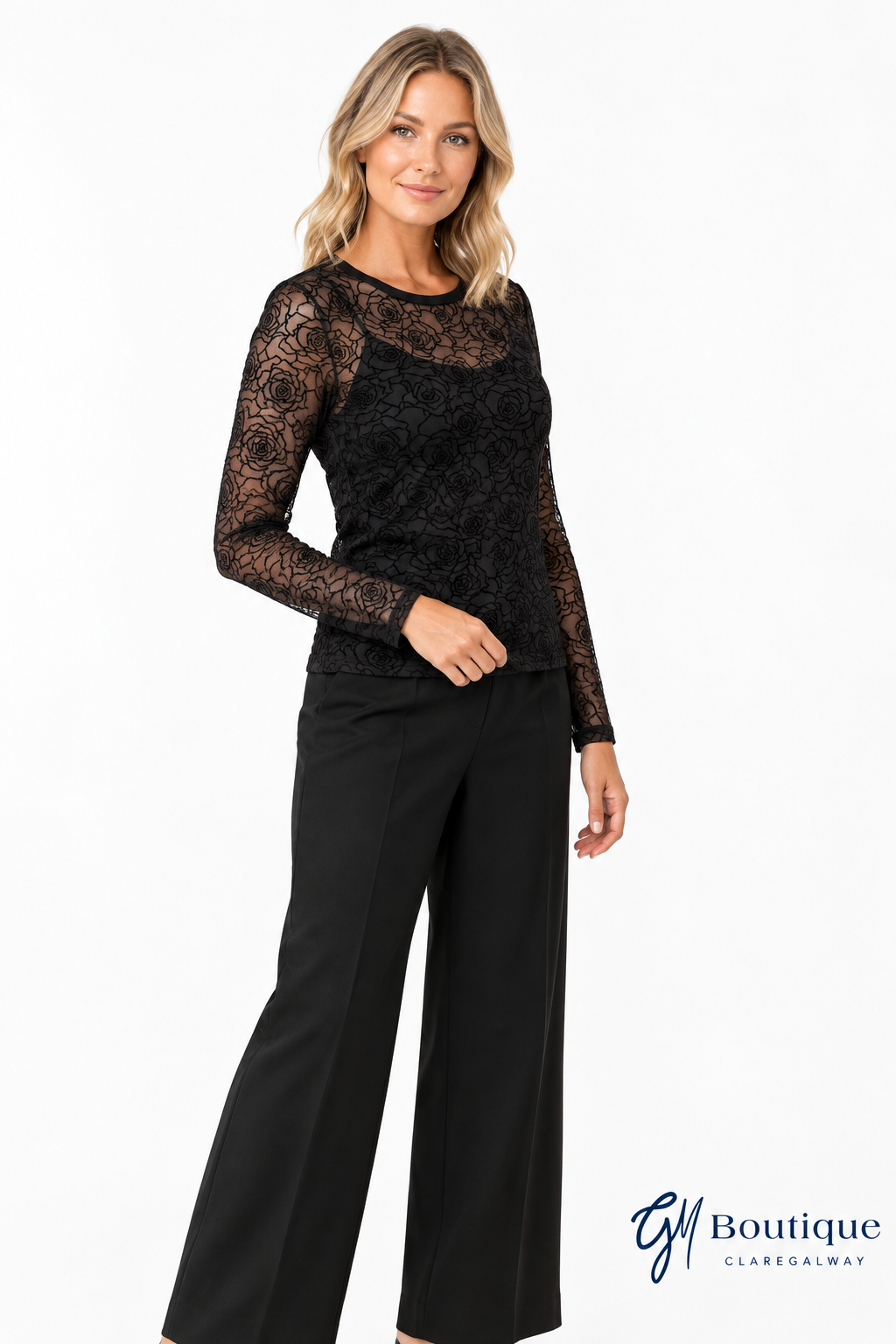 Model in three-quarter pose wearing Mos Mosh MMRose mesh blouse with Oui black tailored trousers and GM Boutique logo 